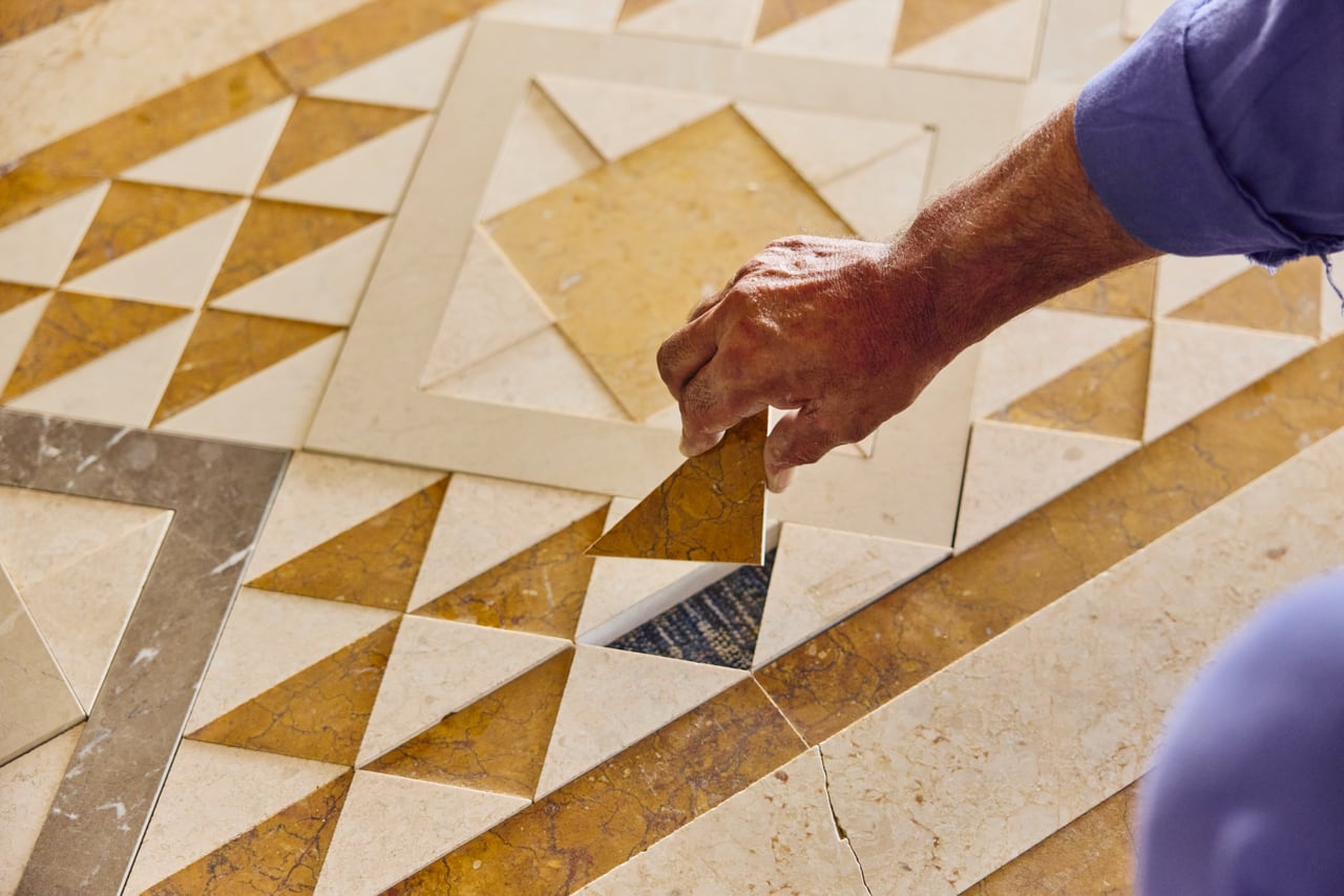 A craftsman setting an inlay piece into a mosaic floor